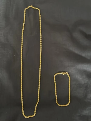 Guldfärgat cordell halsband och armband - Snyggt guldfärgat armband med tvinnad kedja som ger en stilren och trendig look. Armbandet har en enkel karbinhake och passar perfekt för dig som gillar minimalistiska accessoarer. Materialet ser ut som metall med guldfinish. 