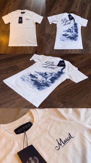 Vit t-shirt från Massif med tryck - Vit t-shirt från Leon Marcel med blått tryck på ryggen som föreställer en vinflaska, vinglas och båt vid kusten. Framtill finns en liten blå logga. Klassisk rund hals och korta ärmar. Perfekt för dig som gillar stilrena plagg med unik design.