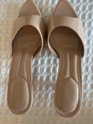 Beige lackade slip-in klackar  - Snygga beige klackar med öppen tå och slip-in modell. Skorna har en bred rem över foten och en smal klack höjd ca 5 cm.  Fick dom som present och vet inte vart dom är ifrån.