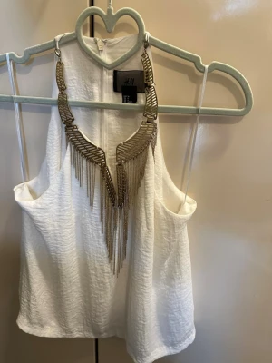 Statementhalsband i guld från H&M - Snyggt statementhalsband från H&M i guldfärgad metall. Halsbandet har geometriska former och långa hängande kedjor som ger en cool och trendig look. Perfekt accessoar för att lyfta vilken outfit som helst med extra edge.
