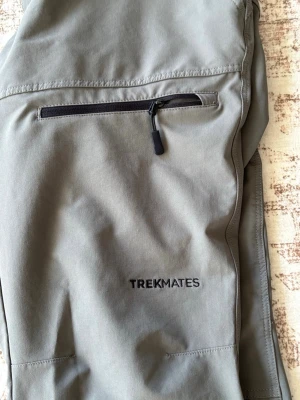 Grå cargobyxor från Trekmates - Snygga grå cargobyxor från Trekmates med dragkedjeförsedd ficka på benet och raka ben. Tillverkade i ett slitstarkt och lätt material som passar perfekt för äventyr och outdoor. Diskret logga på benet och praktiska bälteshällor i midjan.