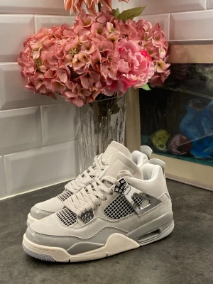 Vita Air Jordan 4 Retro sneakers - Snygga Air Jordan 4 Retro sneakers i vitt och ljusgrått med meshpaneler och detaljer i silver. Skorna har en chunky sula, klassisk snörning och ikoniska plastdetaljer vid snörningen. Perfekta för dig som gillar streetwear och vill sticka ut.