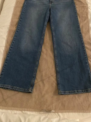 Blå raka jeans med bred passform - Ett par klassiska blå jeans med rak och bred passform. Jeansen har fem fickor, normalhög midja och är tillverkade i denim. Perfekta för en avslappnad och trendig stil.Storlek 32w och längd 30. 