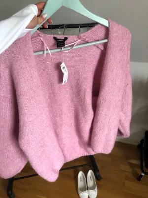Rosa stickad kofta från Lindex - Mysig rosa stickad kofta från Lindex med öppen front och avslappnad passform. Koftan har långa ärmar och är gjord i ett fluffigt, mjukt material som känns skönt mot huden. Perfekt att slänga över en topp för en chill look.