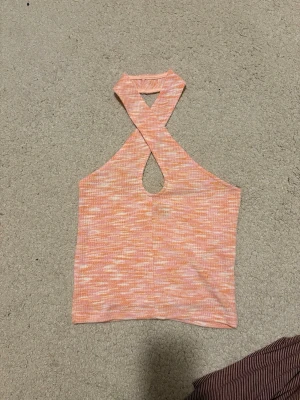 Rosa och orange ribbad halterneck topp - Trendig ribbad halterneck topp från Gina Tricot i rosa och orange toner. Toppen har ett snyggt korsat band framtill och ett litet hål vid halsen. Perfekt för dig som gillar färg och vill sticka ut lite extra.