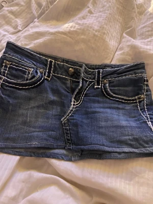 Blå jeansminikjol från LA Idol USA - Säljer en blå jeansminikjol från LA Idol USA med markerade vita sömmar och dekorativa fickor både fram och bak. Kjolen har bälteshällor, knapp- och dragkedjestängning samt coola detaljer på bakfickorna. Perfekt för en trendig streetstyle-look.