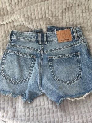 Högmidjade jeansshorts Stradivarius - Säljer ett par blå högmidjade jeansshorts från Stradivarius med vintagekänsla. Shortsen har råa kanter, två bakfickor och bälteshällor. Ljus tvätt! Shortsen är oanvända.