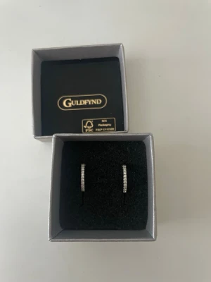 Silverfärgade hoops från Guldfynd - Snygga silverfärgade örhängen i hoop-modell från Guldfynd. Örhängena är dekorerade med små gnistrande stenar längs framsidan som ger en elegant touch. 