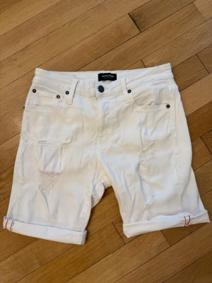 Vita shorts Jack & Jones med slitningar fram - Coola shorts med slitningar på framsidan och röda detaljer på insidan av benskyddet som kommer fram när de är uppvikta (se bild)
