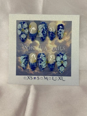 Azure (S);Medium Almond - Unika handgjorda press-on naglar i blått och nude. Naglarna har coolt mönster och handgjorda 3D-blommor i ljusblått med små gulddetaljer. Formen är medium lång almond och designen är handgjord för en riktigt trendig look.S: 15 mm, 11,5 mm, 12 mm, 11 mm, 9 mm 