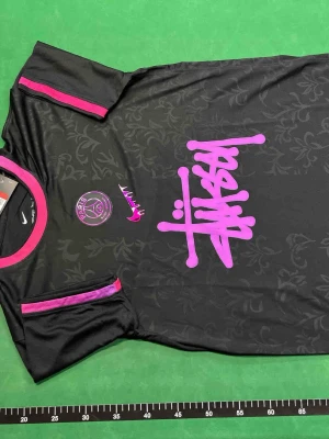Svart PSG Nike Dri-FIT tröja L - Svart sporttröja från Nike med PSG-logga och stora rosa detaljer. Tröjan har Dri-FIT-material som andas, rosa tryck på bröstet och mönstrad yta. Perfekt för fotboll eller träning, med cool design och bekväm passform.