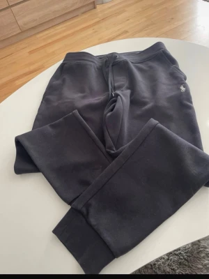 Svarta mjukisbyxor från Polo Ralp Laure - Säljer ett par svarta mjukisbyxor från PRL med dragsko i midjan och ribbade muddar vid benslut. Byxorna har en liten broderad logga på höften och är gjorda i mjukt material som är riktigt skönt att ha på sig.