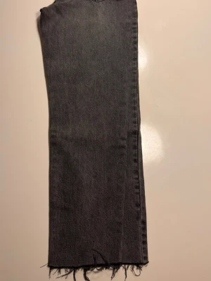 Grå raka jeans med rå kant 28 - Säljer ett par grå jeans med rak passform och trendig rå kant nertill. Jeansen har en klassisk femficksdesign och är tillverkade i denim. Perfekta för en avslappnad och cool stil.