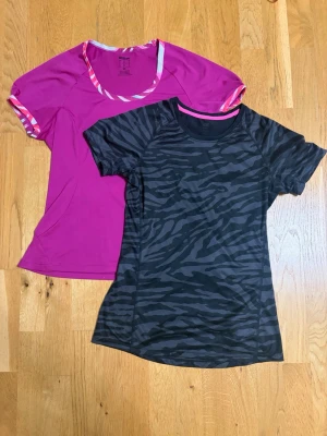 Två sportiga t-shirts i olika färger - Säljer två sportiga t-shirts i funktionsmaterial. En är svart med grått zebramönster och rund hals, den andra är ceriserosa med mönstrade detaljer vid hals och ärmslut. Perfekta för träning eller löpning.