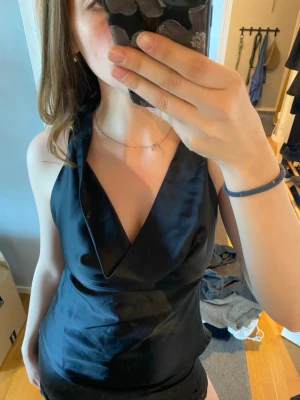 Svart  topp i satin - Snygg svart topp i satinmaterial med djup v-ringning och öppen rygg. Toppen knyts i nacken. M 14+ från Gina Tricot. Aldrig använd bara testad