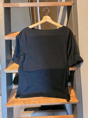Svart båtringad t-shirt med upprullade ärmar från LRL - En stilren svart t-shirt med båtringad hals och uppvikta 3/4 ärmar. T-shirten har en rak passform och är tillverkad i mjukt bomullstyg. Perfekt basplagg för alla tillfällen. Från Lauren Ralph Lauren storlek L