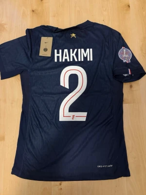 Hakimi #2 – Player Edition (storlek M) - Hakimi #2-tryck. Player Edition med Ligue 1 Winner patch på ärmen. Storlek M. Helt ny och aldrig använd. Säljs i befintligt skick. Skickas snabbt! 🚚💨  Mått för denna tröja (storlek M): (Uppmätta av leverantör – viss variation kan förekomma) • Halva bröstmåttet: 51 cm • Tröjans längd: 72,5 cm • Ärmbredd: 22,5 cm • Axelbredd: 43 cm • Ärmlängd: 39 cm • Manschettbredd: 18 cm  🔥 Player Edition-modell – tajtare passform än vanliga supportertröjor.
