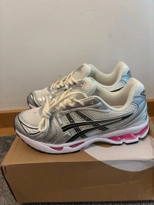 asics gel kayano 14 - Snygga ASICS sneakers i vitt och silver med svarta detaljer och rosa inslag i sulan. Ovandelen är i mesh och syntet för bra andningsförmåga och komfort. Klassisk låg modell med vita snören och vadderad insida för extra skön känsla.
