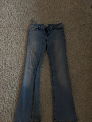 Ljusblå bootcut jeans - Säljer ett par ljusblå bootcut jeans med klassisk femficksdesign och dragkedjegylf. Jeansen har utsvängda ben och är tillverkade i denim med en lätt tvättad look. Perfekta för dig som gillar retrostil och vill ha ett par snygga jeans med skön passform. Nypris var 600