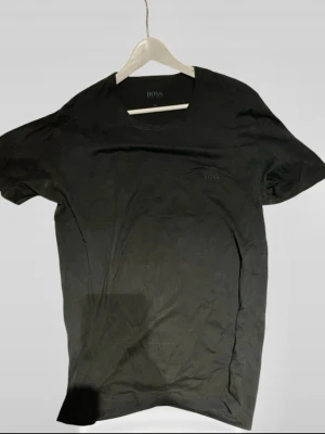 Svart t-shirt från BOSS - Klassisk svart t-shirt från BOSS i fint skick med diskret logga på bröstet. T-shirten har rund halsringning och korta ärmar. Perfekt basplagg i mjuk bomull som funkar till allt.