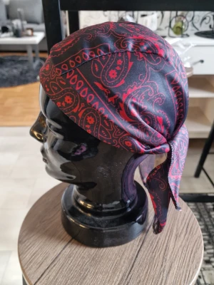 Svart och röd paisleymönstrad bandanas - Snygg bandanasi svart med rött paisleymönster. Tillverkad i ett glansigt, mjukt tyg som ger en skön känsla och sitter bra på huvudet. Knytband bak för justerbar passform. Perfekt accessoar för att lyfta din stil. Bandana pirathatt.  Stretchig snabbtorkande andningsbar och  vindtät. 55-60 cm huvud.