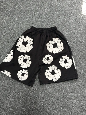 Svarta shorts med vita blommönster - Coola svarta shorts med elastisk midja och stora vita blommönster över hela plagget. De har en avslappnad passform och en bakficka. Perfekta för sommarens alla äventyr.