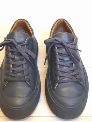 Grå sneakers från Tiger of Sweden - Stilrena grå sneakers från Tiger of Sweden i slätt läder med matchande grå skosnören och diskret logga på plösen. Insidan har en brun kontrastfärg och sulan är tjock och grå för en modern look. Perfekta för dig som gillar minimalistisk och clean stil. Innermått 25,7, stor i storleken. Nypris 2500 kr.