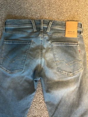 Replay Hyperflex ljusblå jeans - Säljer ett par ljusblå Replay Hyperflex jeans i modellen Anbass. Jeansen har slim fit, klassiska fem fickor och snygga detaljer på bakfickorna. Materialet är stretchigt och bekvämt, perfekt för dig som vill ha både stil och rörelsefrihet. Där fram vid låren så har det blivit en slitning eftersom de slets upp av en gren men jag tycker det ser väldigt snyggt ut med slitningar på! Skriv vid minsta fundering☺️W29 L32