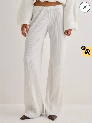 Vita ribbade vida leggings - Säljer ett par vita ribbade leggings med hög midja och vida ben. Materialet är stretchigt och mjukt, vilket ger en skön och avslappnad look. Perfekta att styla med en croppad topp eller oversized tröja. Helt oanvända