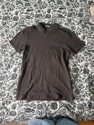 Mörkbrun piké t-shirt - En enkel och stilren mörkbrun piké t-shirt med klassisk krage och korta ärmar. Perfekt till jeans eller shorts för en avslappnad look. Tillverkad i mjuk bomull som känns skön mot huden.