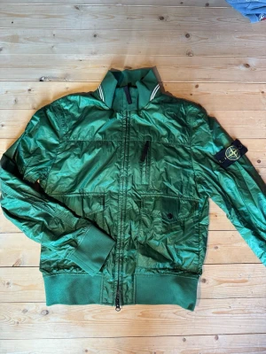 Stone Island Vintage Jacka - Stoneisland Jacka (Micro Rip Stop 7 DEN / Tyvek Shield). En unik jacka i en unik grön metal shimmer färg, säljs pga ej passande storlek, den är i storlek S och skulle säga att den kommer nog passa för person som är 170-180 och väger ca 75kg. Säljs eller byts mot andra SI i göteborgs område. Kom med ett förslag eller skriv PM för mer info.