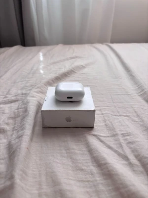 Apple AirPods med laddningsetui - Säljer ett par vita Apple AirPods med tillhörande laddningsetui. Etuiet är kompakt och har en slät, rundad form i blank plast. Perfekta för trådlös musik och samtal, smidig laddning via Lightning-port. Klassisk Apple-design som är enkel att ta med överallt.