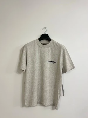 Grå Essentials Fear of God t-shirt  Storlek S och XS - Helt ny Essentials Fear of God t-shirt i grå färg. Design med Essentials-logga på bröstet. Perfekt för både vardag och streetwear. Finns i storlek S och xs
