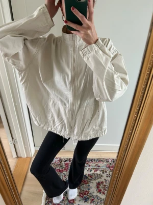 Oversized vit jacka med dragkedja - Säljer en oversized vit jacka med dragkedja framtill och resår i nederkant (har satt dit en säkerhetsnål och vill man ha den tajtare så knyter man en knut!). Perfekt sommar/vår jacka 🩷jag är 171 cm lång! Står inte storlek men skulle tippa på L!