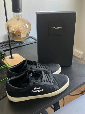 Svarta Saint Laurent sneakers - Snygga svarta sneakers från Saint Laurent med vit sula och handskriven logga på sidan. Pris är diskuterbart, box och dustbag medföljes. Endast använda 1 gång så dom är i ny skick