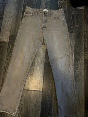 Grå raka jeans från Jack and Jones  - Säljer ett par grå raka jeans från Jack and Jones med klassisk femficksdesign och knappgylf. Jeansen har jag knappast använt 