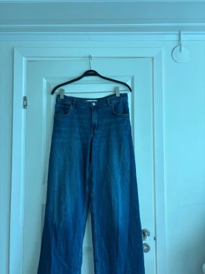 Blå wide leg jeans från Bikbok - Säljer ett par blå baggy jeans från bikbok med låg midja och wide leg-modell. Klassisk femficksdesign och knappgylf. Endast använda några gånger och k superfint skick💕