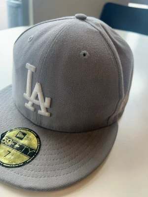 Grå LA New Era 59FIFTY keps - Snygg grå fitted keps från New Era 59FIFTY med LA Dodgers-logga broderad framtill i vitt och MLB-logga bak. Klassisk rak skärm och ventilerande hål upptill. Tillverkad i bomullstyg för en clean och stilren look.
