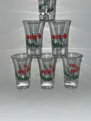 Hot shot tequila 6-pack - Säljer ett set med sex shotglas i klart glas. Glasen har tryck i rött, grönt och svart med orden 'Tequila', 'HOT SHOT' och 'Vodka'. Perfekta till festen eller som samlarobjekt. Klassisk form med lätt utställd kant.