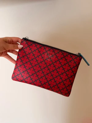 Malene Birger kuvertväska  - Snygg röd kuvertväska från Malene Birger med röd/svart geometriskt mönster och diskret logga framtill. Väskan har dragkedja upptill med blå detalj, likaså bandet som medföljer. Nypris 1100kr❣️❣️❣️