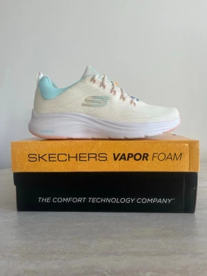 Skechers Vapor Foam sneakers - Snygga sneakers från Skechers med Vapor Foam-teknologi. Skorna är ljusbeige med ljusblå detaljer och har en luftig mesh-överdel samt vita sulor. De har klassiska snörningar och en sportig design som passar perfekt till en avslappnad stil.