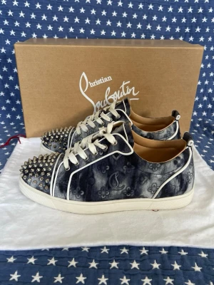Christian Louboutin sneakers med nitar - Unika sneakers från Christian Louboutin i svart och vitt med batikmönster och vita detaljer. Skorna har spetsig tå med silverfärgade nitar och vita snören. Lyxig känsla med läderfoder och ikonisk design. Perfekta för dig som vill sticka ut.Alt ingår på bilderna 