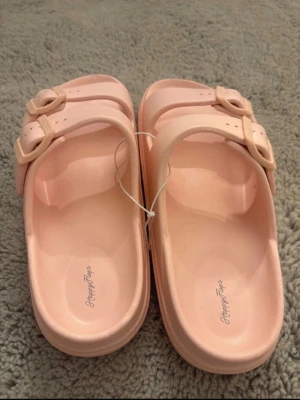 Rosa sandaler från Happy flops - Snygga ljusrosa sandaler från Happy flops med två justerbara remmar och spännen. Tillverkade i syntetmaterial med räfflad sula för extra grepp. Perfekta för sommaren och lätta att ta på sig. Dem är även ny köpta utan prislapp! pris kan diskuteras 