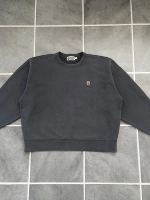 Sweatshirt från BAPE - A Bathing Ape - Mörkgrå sweatshirt från BAPE med rund halsringning och liten broderad logga på bröstet. Tröjan har en klassisk passform med ribbade muddar vid ärmslut och nederkant. Perfekt för en avslappnad och stilren look. Passar oversized 