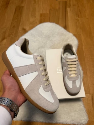 Margiella gats beige/vit - Skor i vitt och beige med ovandel i läder och mocka, samt klassisk gummisula. Snygg retrostil med beige snörning och diskreta detaljer. Perfekta för dig som gillar minimalistisk och stilren design.