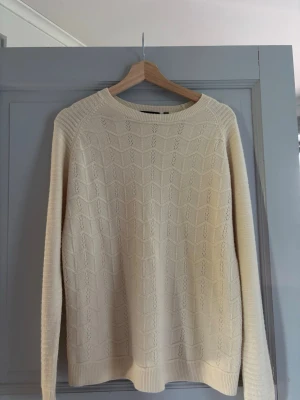 Beige stickad tröja - Säljer en beige stickad tröja från Cashmere-Feeling i storlek M. Tröjan har ett diskret mönster, rund halsringning och ribbade muddar vid ärmslut och nederkant. Materialet är mjukt och ger en lyxig känsla, perfekt för kyliga dagar.
