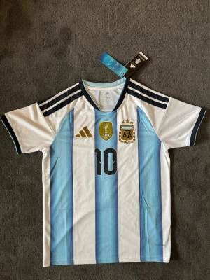 Argentina VM 26/27 hemma Messi 10 - Fotbollströja med Messi på ryggen. Tröjan är helt ny med tagg kvar och i perfekt skick. Perfekt för dig som är supporter, samlar på fotbollströjor eller vill ha en snygg tröja till träning och vardag.                                                                      ⚪ Skickas inom 24 timmar.                                         Vid intresse eller frågor är det bara att skicka 👍