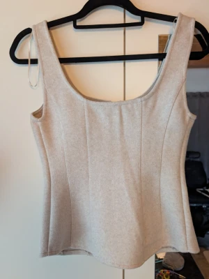 Beige linnetopp med söm-detaljer - Snygg beige linnetopp med markerade sömmar som ger en figurnära siluett. Toppen har breda axelband och rundad halsringning. Perfekt att styla med jeans eller kjol för en clean look.