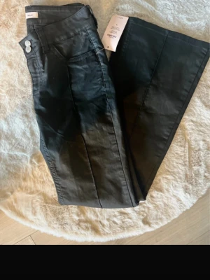 Svarta utsvängda jeans från Nelly - Säljer ett par svarta jeans från Nelly med hög midja och utsvängda ben. Jeansen har dubbla silverknappar i midjan och markerad söm framtill. Materialet är stretchigt och ger en snygg passform. Perfekta för en trendig look. Ny pris 699 säljer för 500 kr.