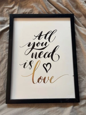 Tavla med text All you need is love - Snygg tavla med svart ram och vit bakgrund. Texten 'All you need is love' är skriven i svart och guld med ett hjärta. Perfekt som dekoration till sovrum eller vardagsrum.25*35